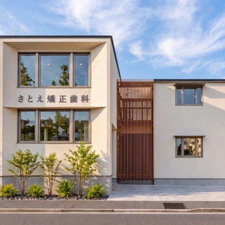 Modern white two story building with large front windows Japanese sign on facade reads さとえ矯正歯科 and a wooden lattice feature separates sections 神戸市の注文住宅